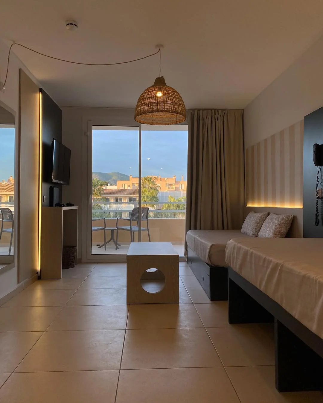 Suite de hotel con cabecero revestido, balcón y lámpara de mimbre